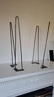 Four bent-steel hairpin-style table legs displayed on top of a white surface, showing overall condition and design.