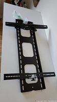 Full view of the black metal TV wall mount showing mounting holes and included hardware in plastic bags.