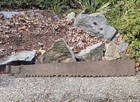 Full view of the rusty antique saw blade laid on the ground against rocks.
