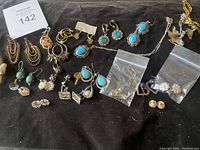 Full view of assorted earrings and pendants including turquoise stone jewelry, gold and silver-tone items, with some in small plastic bags.