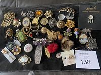 Full view of the assortment of various vintage style pins, brooches, and hair accessories laid out on black fabric.