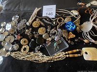 Overview of the assorted jewelry laid out on black fabric including necklaces, brooches, earrings, scarf clips.