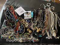 Wide view of assorted necklaces and bracelets laid out on a black cloth, showing a variety of beads, chains, bangles, and pendants in multiple colors and styles.