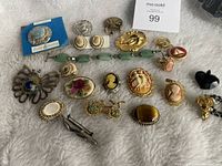 Overview of assorted pins, pendants, cameo brooches and earrings laid out on a fabric surface.