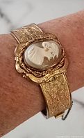 Bracelet worn on wrist showing central oval cameo and embossed floral detailing.