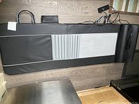 Black full body massage mat lying flat with attached cushion and folding design on wooden floor.