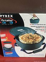 Photo of the Pyrex Portables hot and cold food carrier set box showing the carrying case open with a 4.5L clear glass container filled with baked pasta inside.