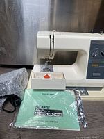 Overall profile of the Kenmore sewing machine with power cord, foot pedal, and owner's manual displayed in front on table surface.