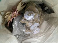View inside large white bag showing handmade lace and burlap dolls with decorative buttons and lace accents, tied with twine and pink ribbon.