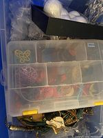 Overview of blue plastic tote with plastic organizer box on top holding various jewelry components and small items inside compartments. Below organizer, assorted jewelry and supplies are visible.