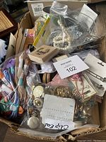 Top view of box containing embroidery floss skeins, assorted buttons, jewelry clips, faux pearls, and boxed crochet kit.