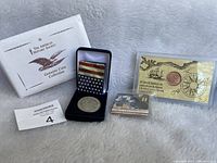 Lot of 3 collector coins including a silver-tone Apollo 11 coin in a blue velvet box, a Captain Cook replica coin with certificate, and a smaller coin with mission card.