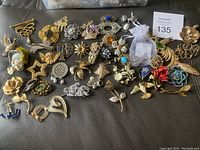 Overview photo showing all costume jewelry pins with a variety of designs laid out on a dark surface.