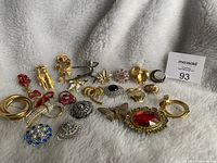 Photo showing assortment of 20 pins and brooches in varied styles including floral, figurative, and abstract designs with gold and silver tones.