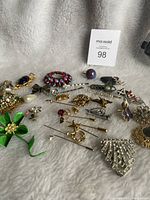 All assorted pins, hair pins, and brooches laid out on a soft textured fabric showing various designs and colors