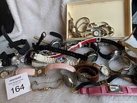 Multiple vintage wristwatches laid out on soft white fabric showing different styles, bands, and faces.
