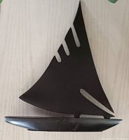 Side view of the black metal sail boat sculpture showing the tall sail with cut-outs and the base of the boat.