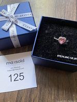 Sterling silver ring with pink heart-shaped crystal in black velvet box and blue branded box with ribbon.
