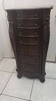 Front view of dark wood jewelry armoire with closed drawers