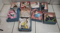 Nine vintage Madame Alexander dolls in original blue boxes with tissue paper on tiled floor, showing overall lot condition and packaging.