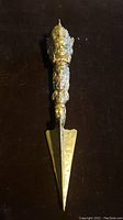 Full view of the brass phurba showing dagger blade and handle with triple-headed deity figures