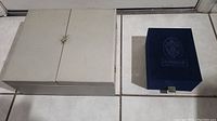Closed beige cardboard box for fine china tea set next to closed Faberge blue display box.