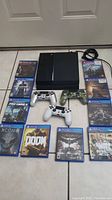 Overhead view showing PS4 console, three controllers, power cable, and multiple game cases.