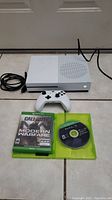 White Xbox One S console, controller, Call of Duty Modern Warfare case and Halo disc on tile floor