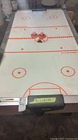Top view of air hockey table showing playing surface, two pink paddles and one puck, with dimensions labeled.