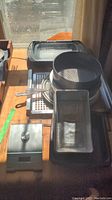 Photo of multiple baking pans and mesh sifters stacked on a wooden surface near a window.