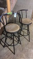 Two black metal bar stools with beige cushioned swivel seats shown together from a slightly angled perspective.