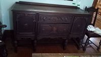 Front view of dark oak hand-carved buffet showing two cupboards and two drawers, ornate carving and turned legs