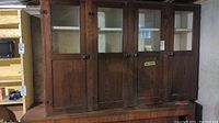 Full view of antique wood china cabinet showing five doors with glass on the dining room side and solid panel doors on the pantry side.