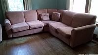 Full view of the three piece sectional couch in light brown upholstery with two throw pillows on a wooden floor near windows