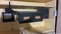 Small black older model TV on left, black metal card box center bottom shelf, and black Micromax heater on right top shelf.