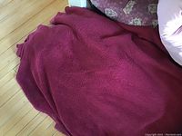 Red fleece throw blanket folded on wooden floor with pillows around it