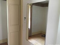Rectangular vintage wall mirror hanging on a beige wall reflecting part of a window with curtains and a wooden floor.