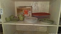 Photo showing boxed Jeannette punch bowl set, green plastic tea set with cups, saucers, plates, and assorted plates on shelf.