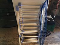 White metal drying rack with purple plastic connectors for drying clothes next to a blue metal wire bundle buggy with wheels.