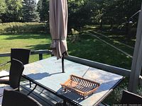 Full view of patio table with folded tan umbrella in center and outdoor chairs around it on wooden deck