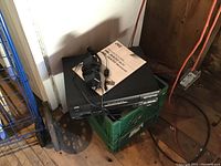 JVC VCR player with power cable and original box, located next to a green crate and other items on floor indoors.