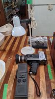 Photo showing black and chrome Bolex 280 microzoom camera with wrist strap beside a white lamp.