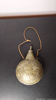 Full front view of circular brass flask with leather strap
