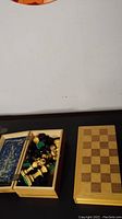 Wooden folding chess board next to a box of wooden chess pieces on a black surface