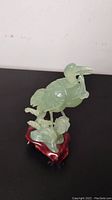 Front view of green jade whooping crane sculpture on wooden base showing detailed carving and bird posture.