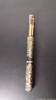 Close-up view of the lower brass holder containing the chopsticks, showing detailed engravings and condition.