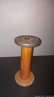 Side view of the vintage oak sewing bobbin showing the wooden middle shaft and metal ends.