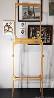 Full view of the folding wooden art easel against a wall with artwork behind it.