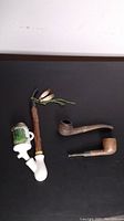 Top-down photo of three vintage German pipes showing porcelain stein pipe, traditional wooden pipe, and rustic decorated wooden pipe.