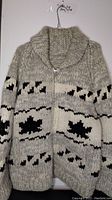 Full view of the beige hand knitted men's sweater with black geometric patterns and zipper front
